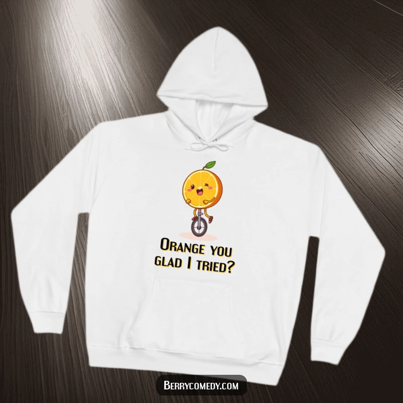 Funny hoodie art of a happy orange slice with wobbly legs, comically attempting to ride a unicycle, perfect for cozy, inspiring wear.